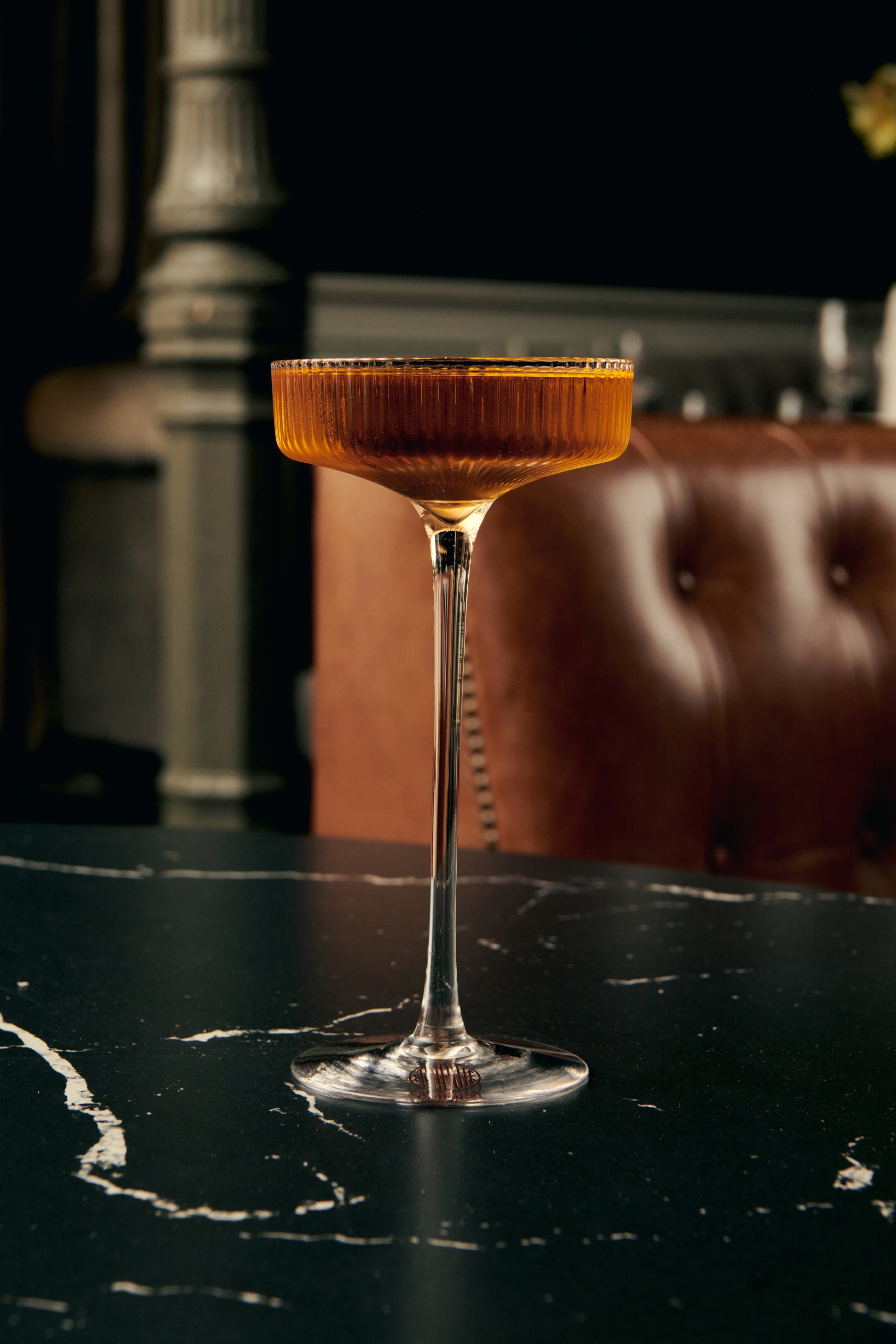 LE Tribute cocktail served in a ribbed crystal coupe glass on a black marble table, luxurious presentation