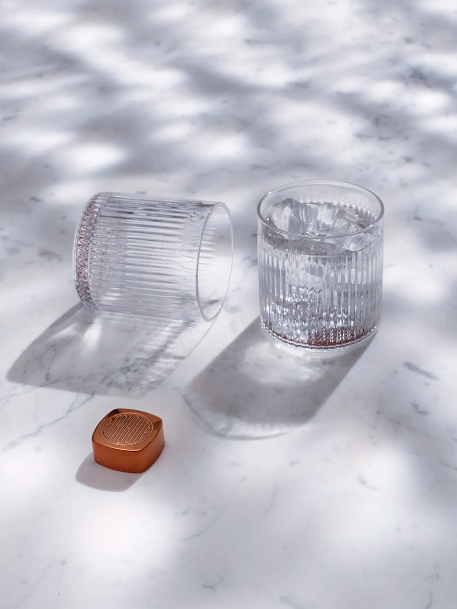 LE Tribute branded crystal glasses and copper accessory, presented on a marble surface with light and shadow play