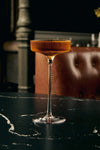 LE Tribute cocktail served in a ribbed crystal coupe glass on a black marble table, luxurious presentation