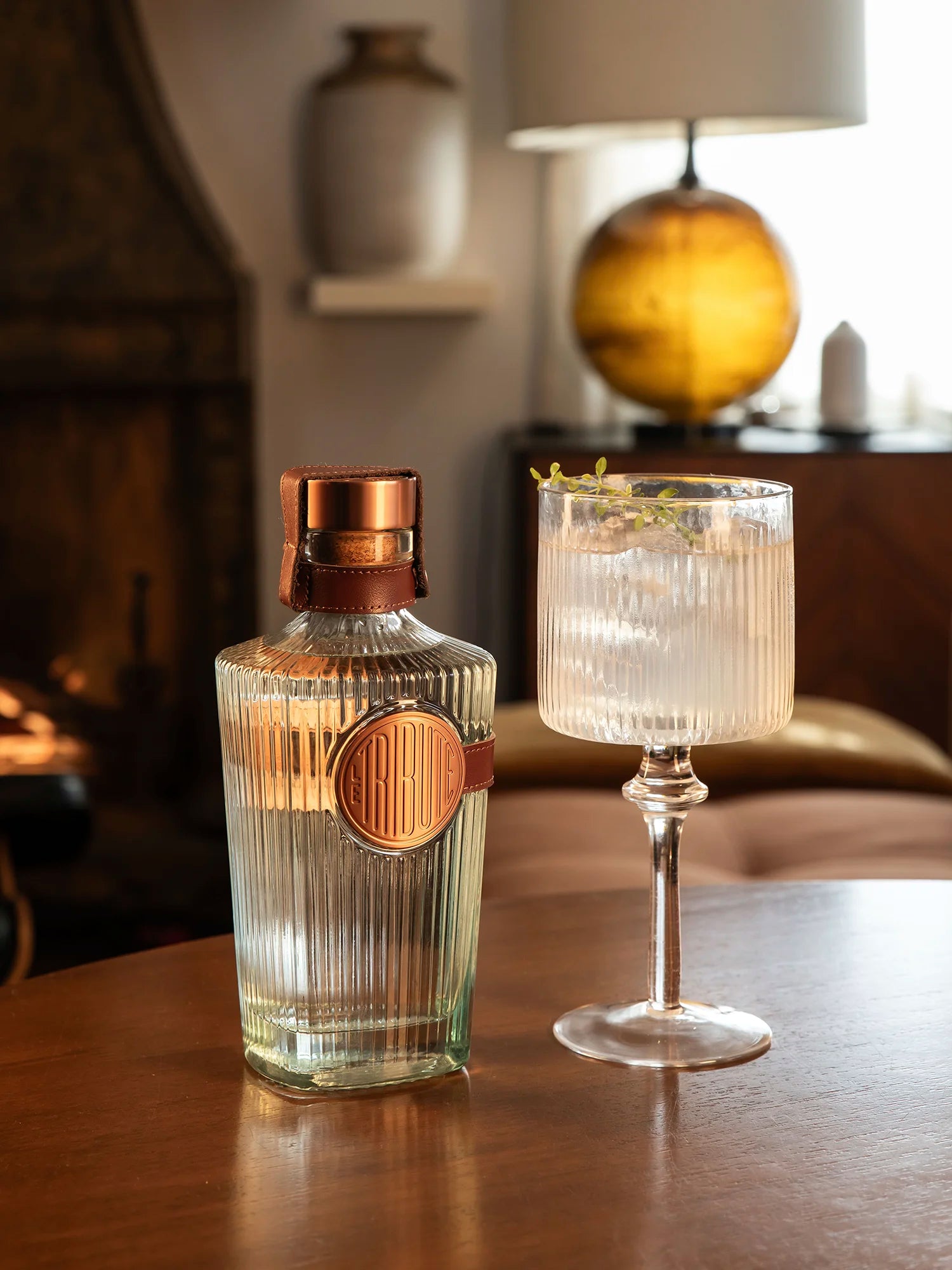 LE Tribute gin bottle with a refreshing cocktail in a crystal glass, styled in a cozy interior setting