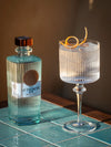LE Tribute Gin bottle paired with a classic gin cocktail garnished with orange peel, on a textured blue surface